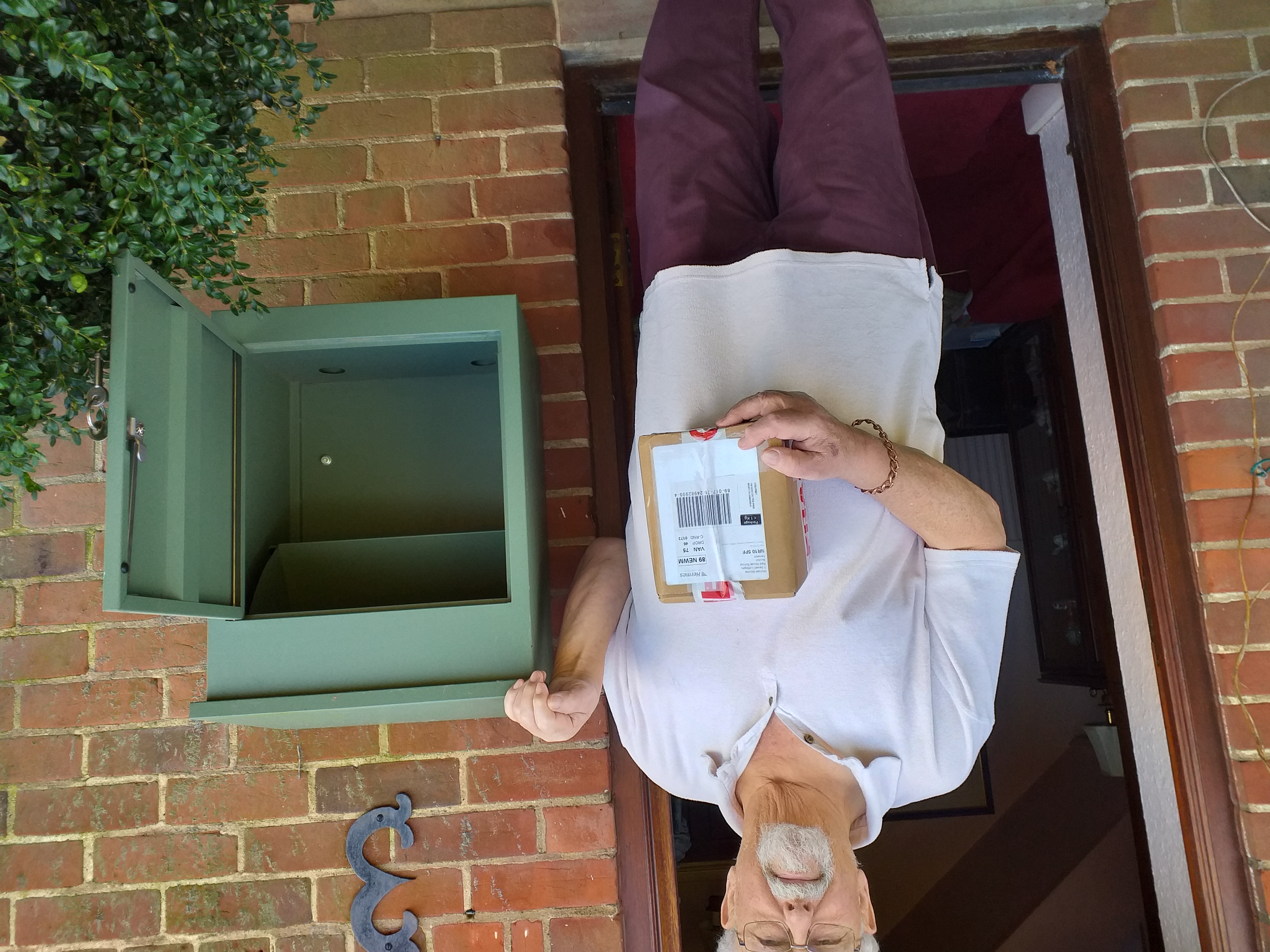 A pleased old man holding a parcel, next to green Smart Parcel Box